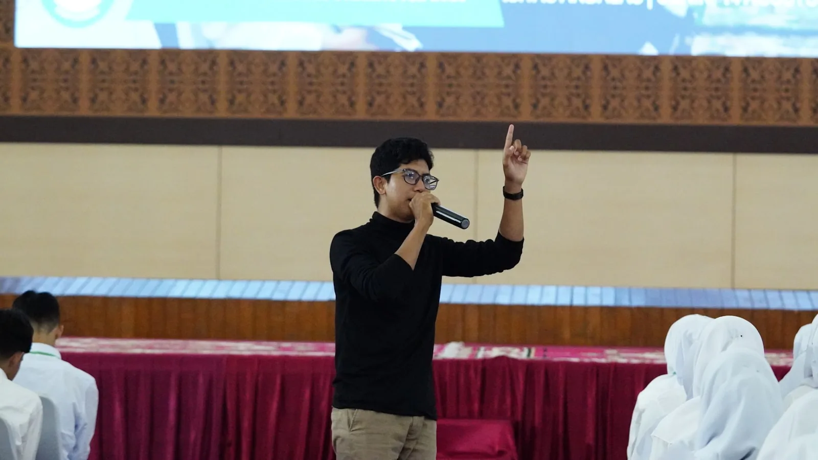 A speaker talks into a microphone on stage in front of a seated audience.